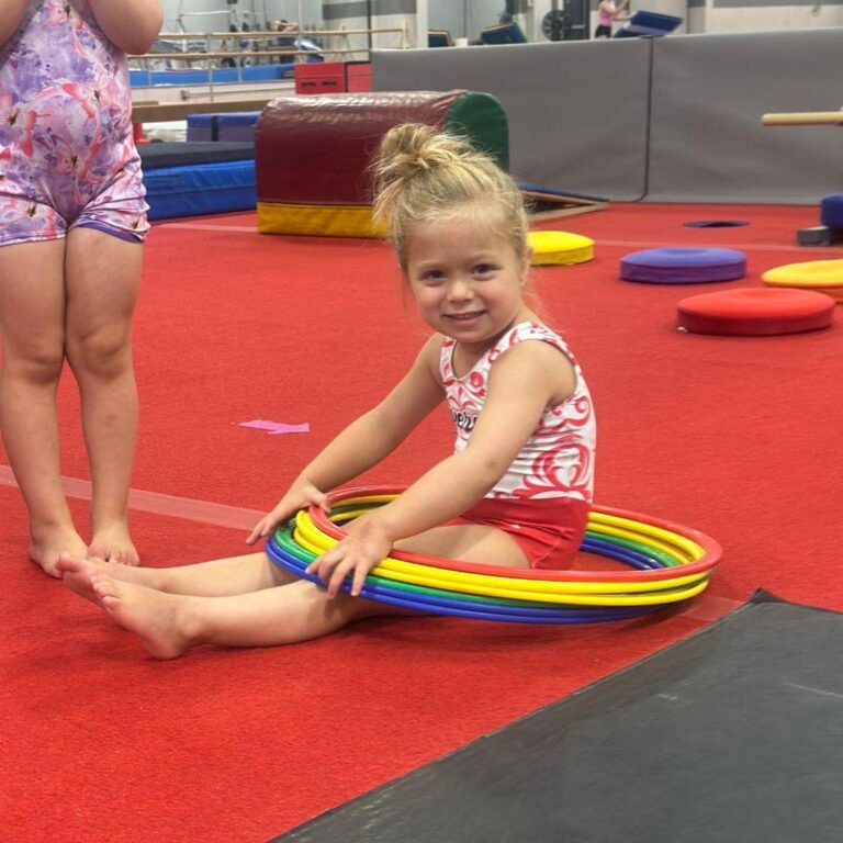 Preschool gymnast sitting on a red carpet.